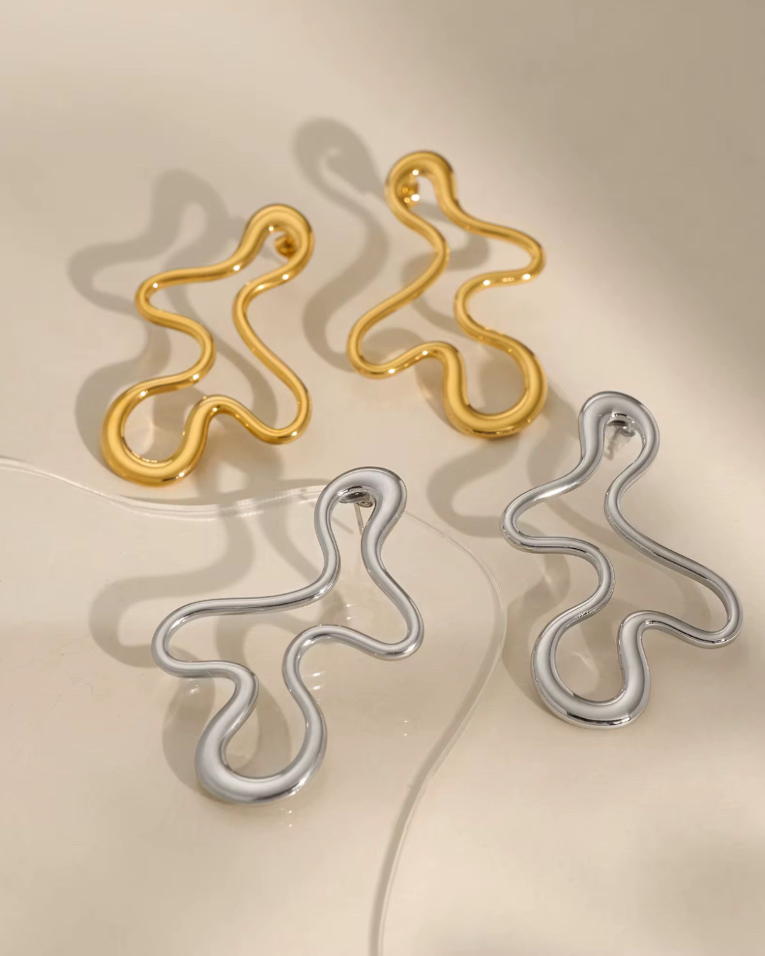 Abstract Baddie Earrings in gold and silver shown together. A bold lifestyle jewelry photo highlighting luxury sculptural hoops for women with modern artsy style.