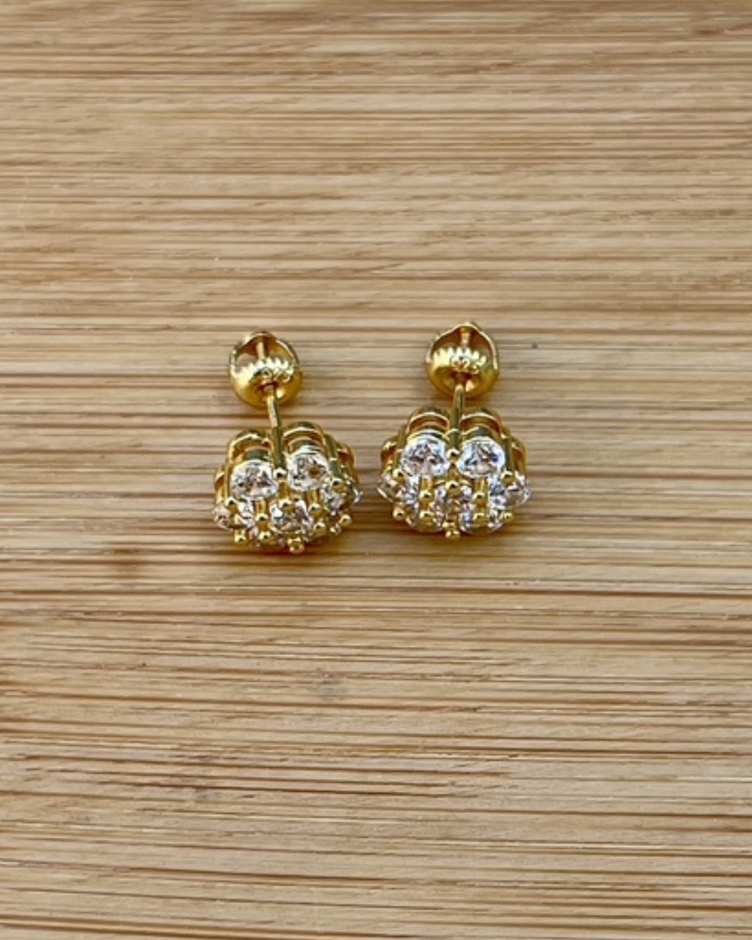 Gold CZ flower cluster stud earrings displayed on a wood surface. Timeless floral studs that have screw backs to help with safe keeping.