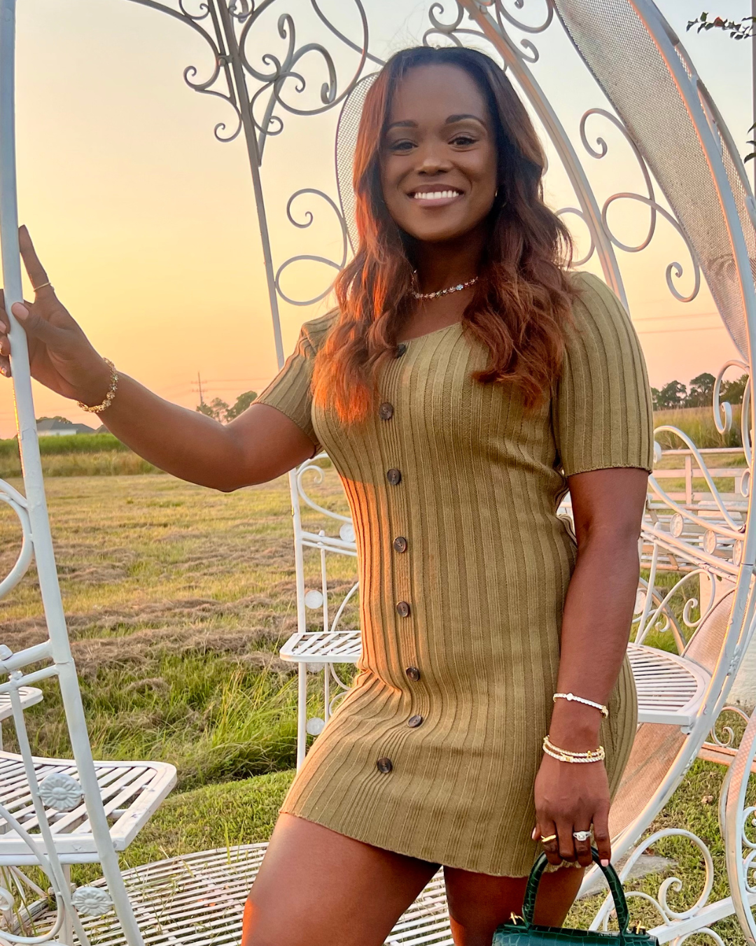 CEO of I Am Luxury Accessories Boutique smiling at sunset wearing the In Full Bloom Bracelet stacked with gold jewelry, paired with the matching In Full Bloom Necklace, styled with a ribbed dress and handbag for an elegant outdoor look.