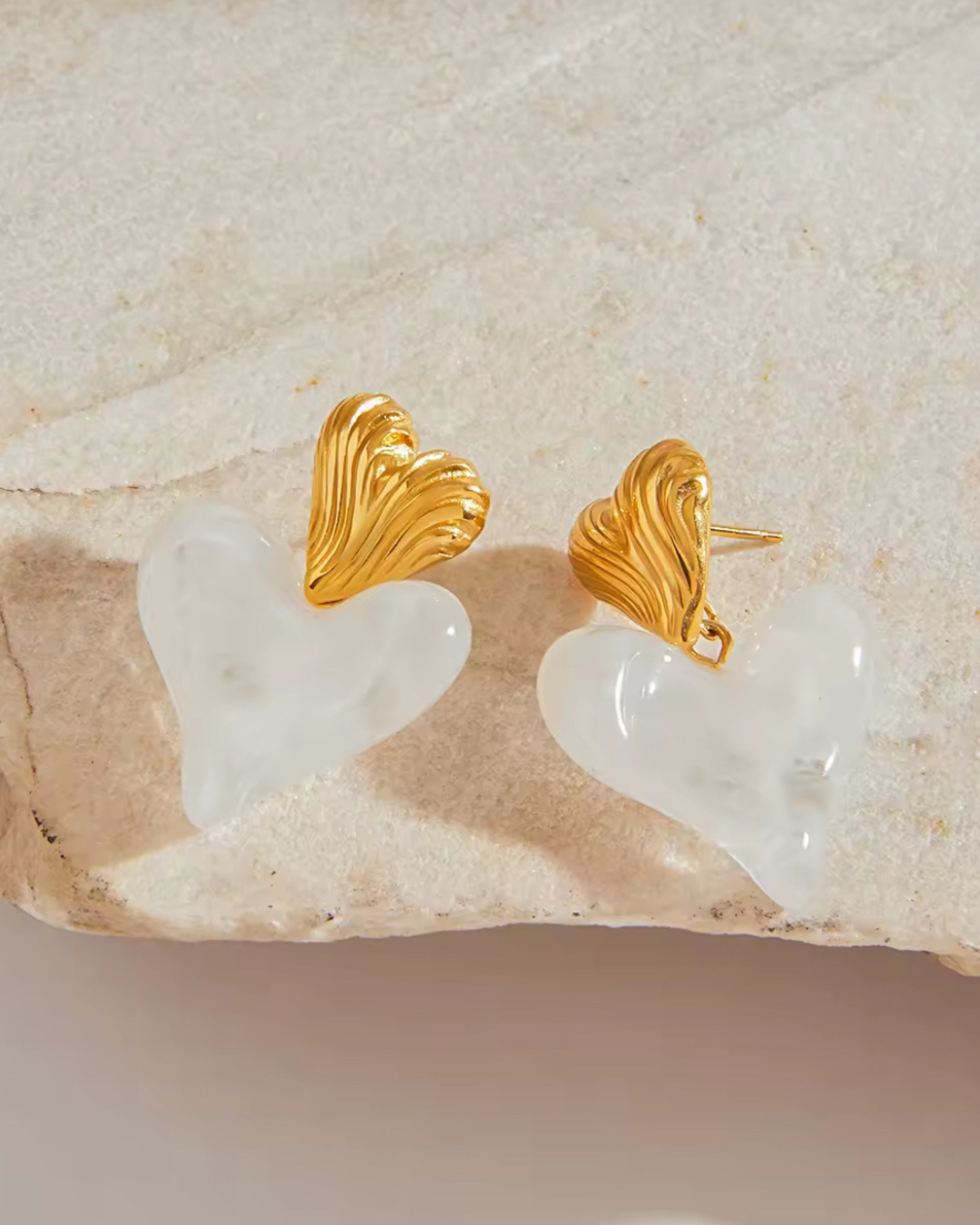 Love on Top earrings in white and gold with sculpted double heart drop design, displayed on stone background as luxury lifestyle jewelry for women.
