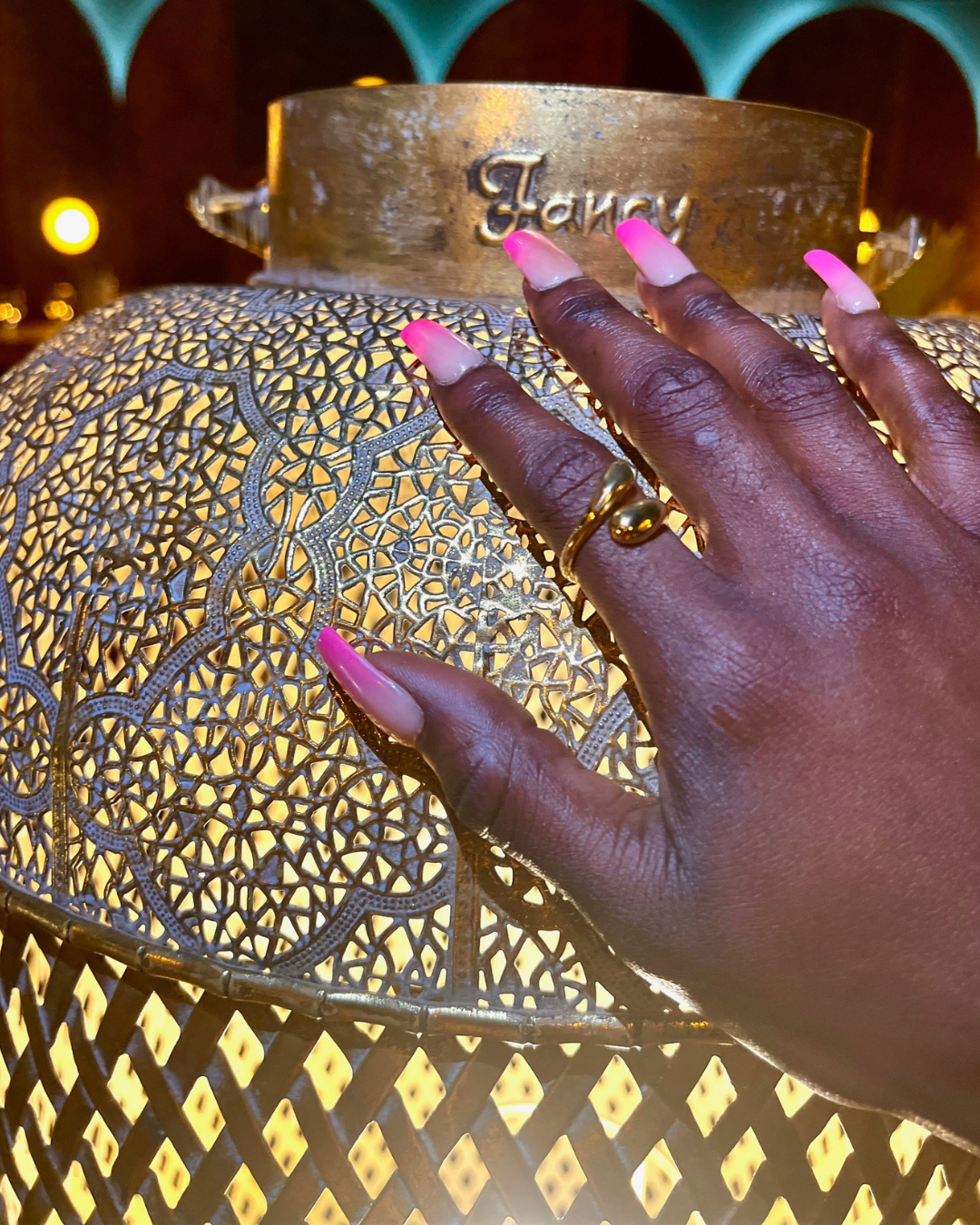 Glossy gold sculptural ring worn on a glowing hand, styled against a luxe mosaic-patterned lantern. The perfect everyday statement for vacation-ready minimalists.