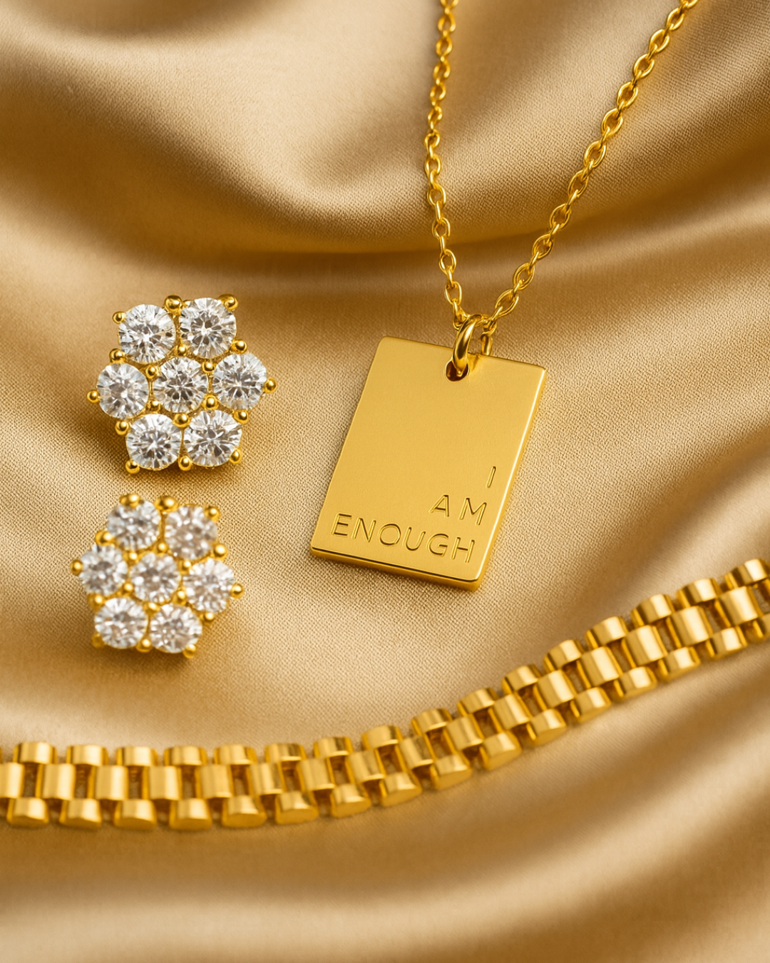 The Luxe Affirmation Set featuring the gold I Am Enough Necklace, 7-stone All-Star CZ stud earrings, and SneakyLink gold link bracelet on satin background.