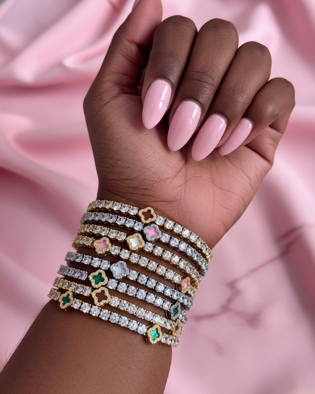 Hand wearing multiple diamond bracelets on a pink satin background