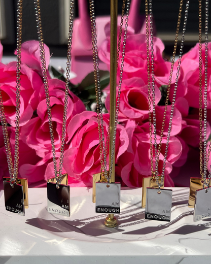 Multiple I Am Enough necklaces in gold and silver shine boldly against pink roses, styled to affirm self-worth and remind women everywhere that they are more than enough--every single day. 