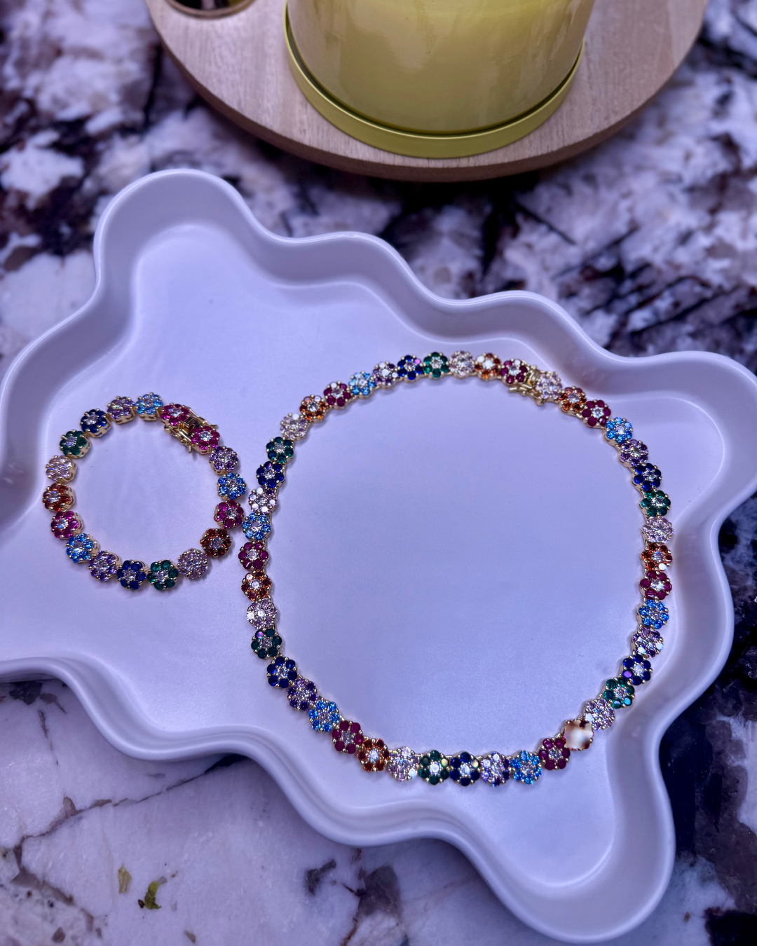 In Full Bloom Necklace in 18k gold stainless steel with multicolor CZ floral clusters, displayed on a white tray with the matching In Full Bloom Bracelet on a marble background.