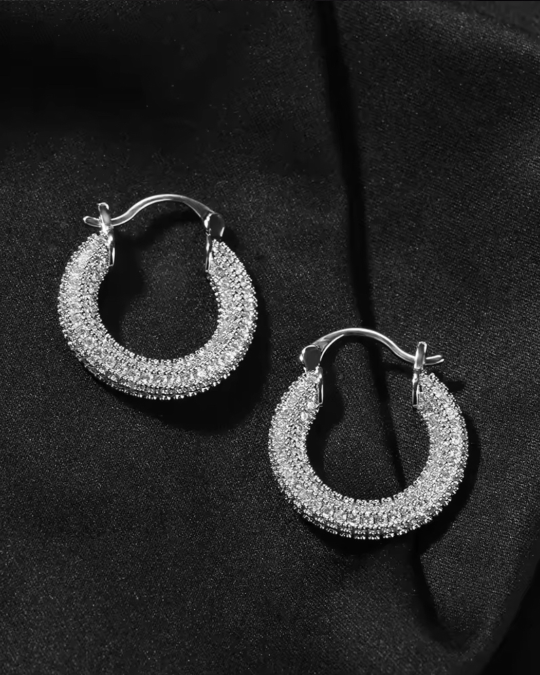 Silver Main Character Earrings with CZ stones, bold hoop design perfect for formal fashion looks, displayed on a black fabric background.