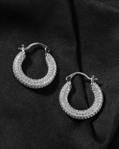 Silver Main Character Earrings with CZ stones, bold hoop design perfect for formal fashion looks, displayed on a black fabric background.