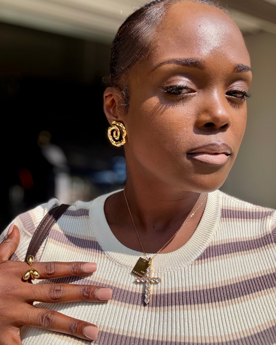 CEO of I Am Luxury Accessories Boutique wearing the Modern Muse Ring in gold, a sculptural open tear-drop design, styled with striped knitwear, layered gold necklaces, and the Twist of Faith Earrings.