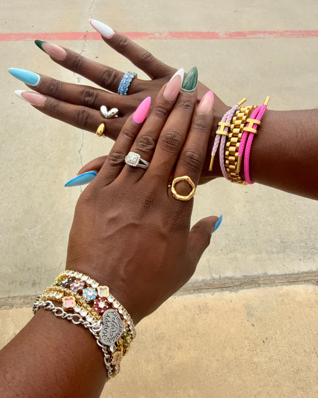 Two hands adorned with colorful manicured nails, stacked bracelets, and multiple rings, featuring the Opulence 18k gold-plated oval-shaped ring as the focal point.