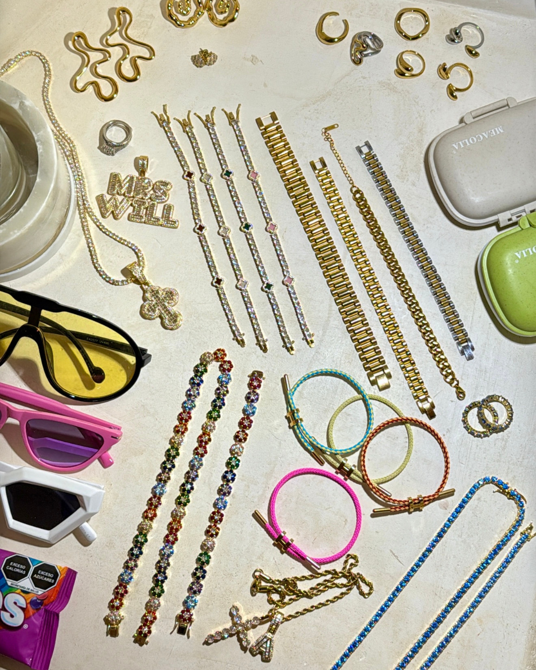 Flatlay of jewelry from the Summer Luxe In Bloom campaign photoshoot in Tulum, featuring colorful Stacked Like a Horse Bracelets, In Full Bloom Bracelets, gold link bracelets, rings, and layered necklaces styled alongside sunglasses and accessories.
