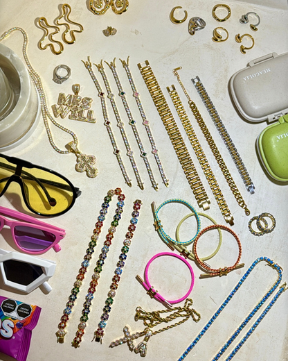Flatlay of jewelry from the Summer Luxe In Bloom campaign photoshoot in Tulum, featuring colorful Stacked Like a Horse Bracelets, In Full Bloom Bracelets, gold link bracelets, rings, and layered necklaces styled alongside sunglasses and accessories.