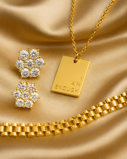 The Luxe Affirmation Set featuring the gold I Am Enough Necklace, 7-stone All-Star CZ stud earrings, and SneakyLink gold link bracelet on satin background.