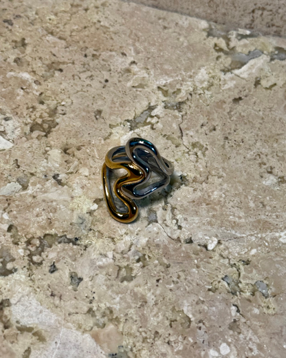 Untamed Ring in intertwined gold and silver metals, displayed on stone, capturing a resort-style aesthetic perfect for vacation and tropical getaways.